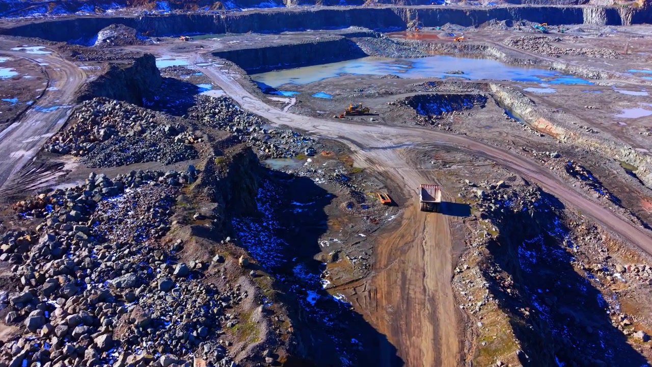 Quarry landscape with mining machinery. Aerial drone shot of dump truck, rock piles and turquoise ponds across the open pit.