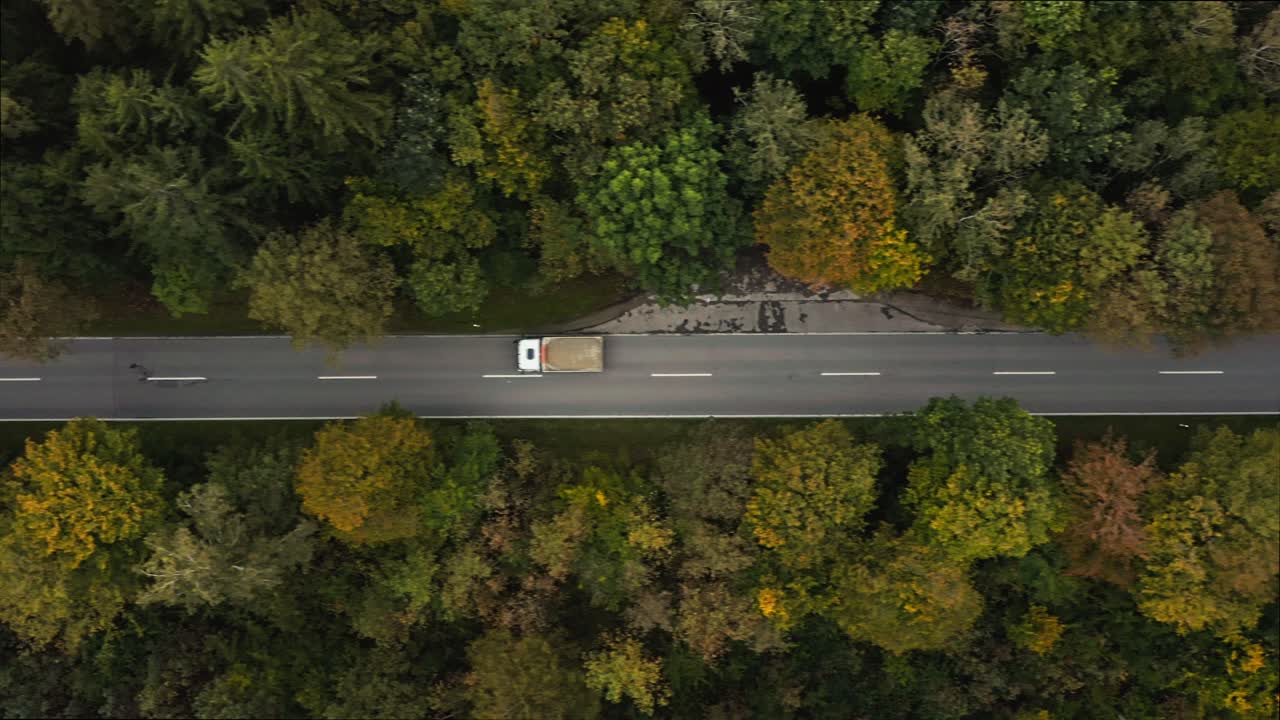 A fast driving lorry at a straight road in a autumn colored forest street, filmed from above by a drone