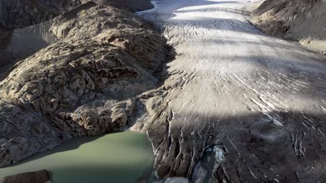 Vista-Aérea-Del-Glaciar-Del-Ródano-Cerca-Del-Paso-De-Montaña-De-Furka-En-La-Frontera-De-Valais-Y-Uri-En-Suiza-Con-Una-Bandeja-Desde-El-Hielo-Hasta-El-Lago-Glacial-Lleno-De-Icebergs