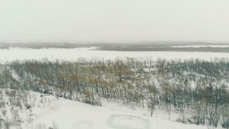 Schneebedeckter-Berg-Am-Kahlen-Wald-Und-Luftaufnahme-Des-Gefrorenen-Flusses