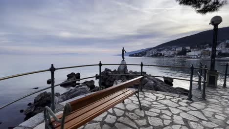 Statue-Einer-Frau-Auf-Der-Bank-Der-Ferienortinsel-Am-Meer-In-Der-Ferne-Näherte-Sich-Lovran,-Opatija,-Kroatien