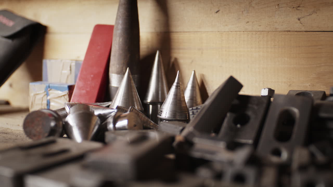 Close-up shot of various metal lathe centers, cones, and heavy machining step blocks stored on a rustic wooden shelf