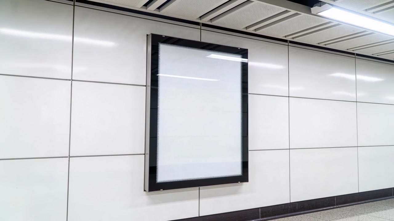 Panning camera revealing lit ad lightbox on tiled station wall, showing blank face and reflections