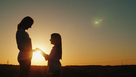 mom and daughter hold hands look at each other silhouettes at sunset 4k video