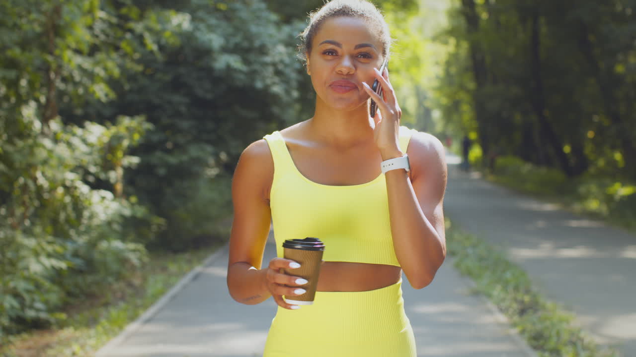 Donna che cammina nel parco, parla al telefono e beve caffè