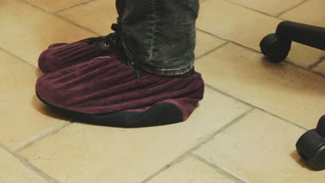 man slipping protective fabric covers over shoes in home setting. close-up. safety measures, personal protection and preventive healthcare practices.