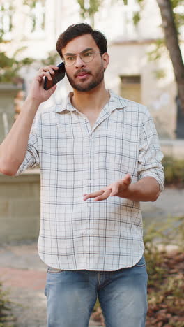 Joven-Hispano-Enojado-Y-Furioso-Discutiendo-Mientras-Habla-Por-Teléfono-Inteligente,-Irritado,-Gritando,-Peleando-Al-Aire-Libre