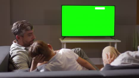 father talking with boy while watching tv with family