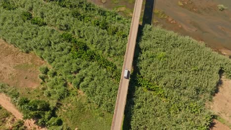 Aerial-top-down-view-of-white-van-drives-on-asphalt-bridge-in-rural-Madagascar-countryside