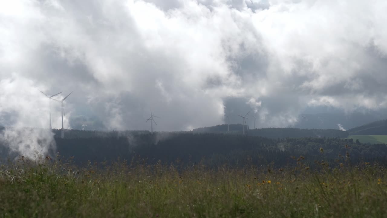 Cloudy day with wind turbines on a distant mountain, surrounded by green meadows