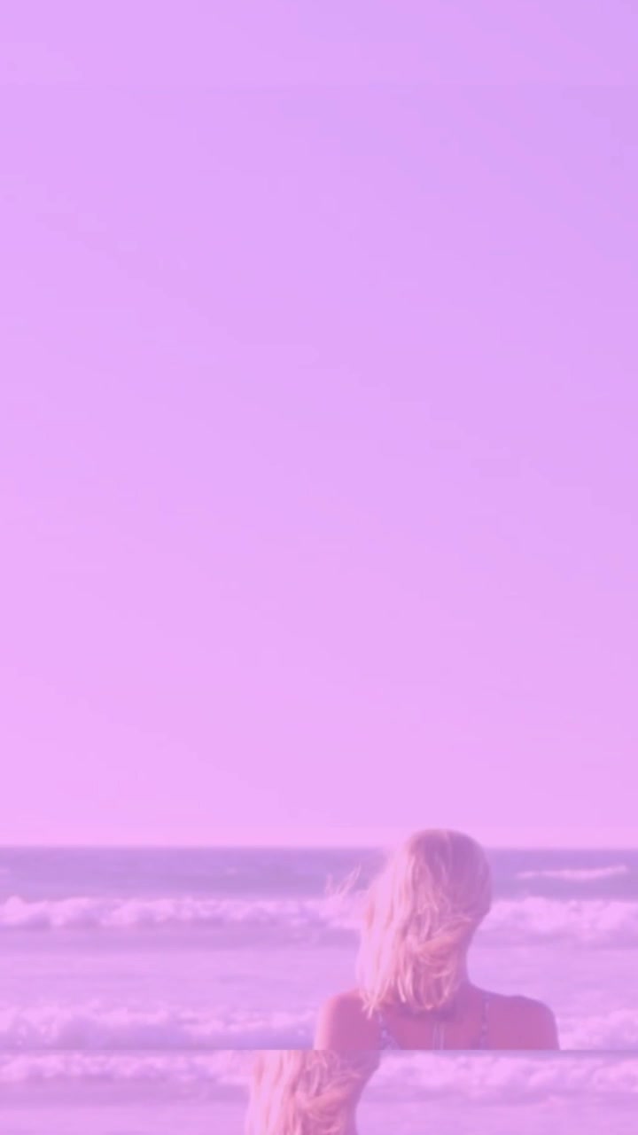 柄物のキャミソールとデニムのショートパンツを着用して岸辺で水平線を眺める女性。太陽のフレアが現れる。