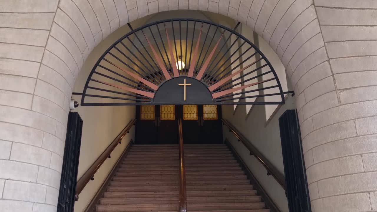 Entrance to a modern Christian church in central Stockholm, with stairs ascending beneath a prominent golden cross