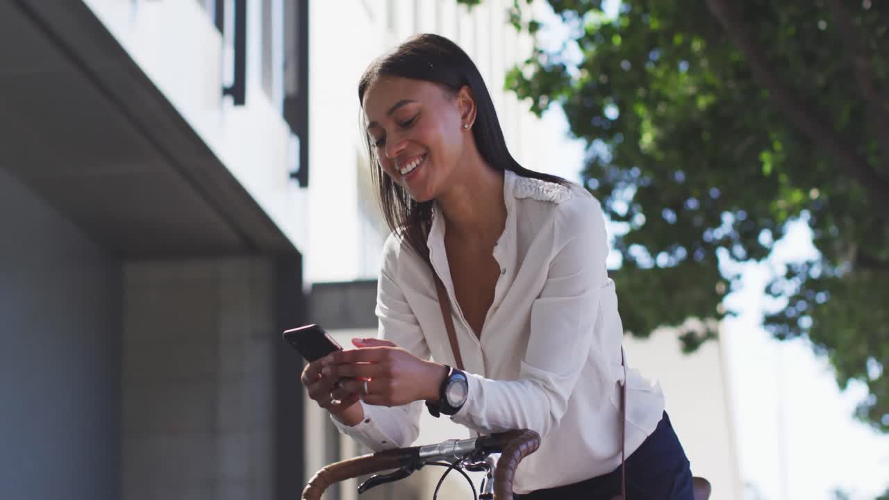 African american woman using smartphone leaning on bike in street