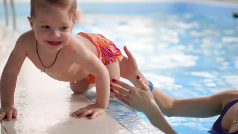 mom helps baby to get on the side of the pool during swimming training for babies