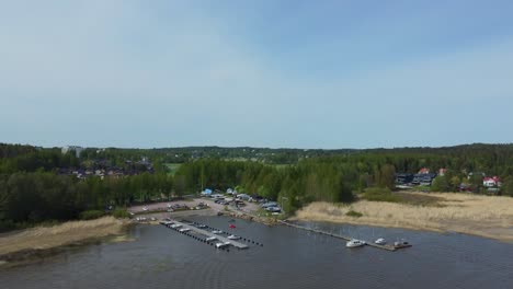 The-scene-reveals-a-small-dock-where-boats-gently-sway-on-the-water's-edge,-surrounded-by-a-beautiful-landscape-of-a-forest-and-a-charming-town