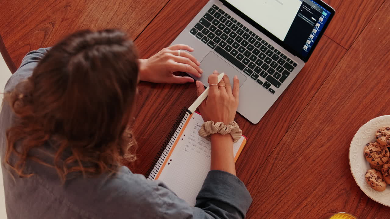 Vista superior de mujer escribiendo en un cuaderno mientras usa una computadora portátil