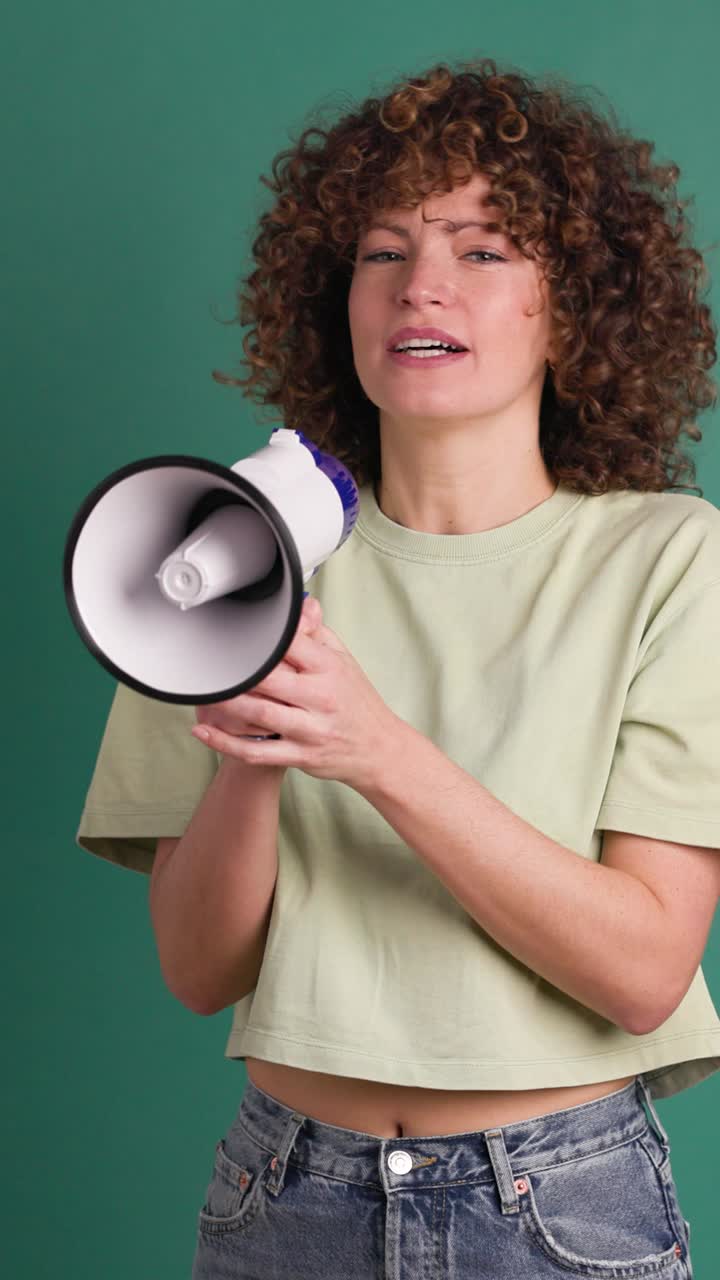 Excited young woman screaming on loudspeaker in green studio. Vertical footage