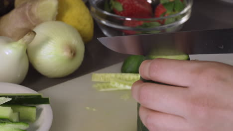 cutting fresh green cucumber into four portions with a knife in the kitchen - closeup shot