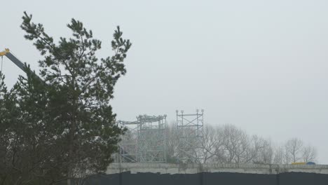 Intensive-work-on-the-construction-site-located-near-the-coast-of-the-sea,-large-mobile-crane-moving,-overcast-day-with-fog,-distant-wide-shot