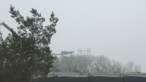 trabajo intensivo en el sitio de construcción situado cerca de la costa del mar, gran grúa móvil en movimiento, día nublado con niebla, tiro ancho lejano