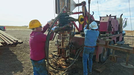 drilling equipment is prepared for work. two men install the machinery to extract oil in the field.