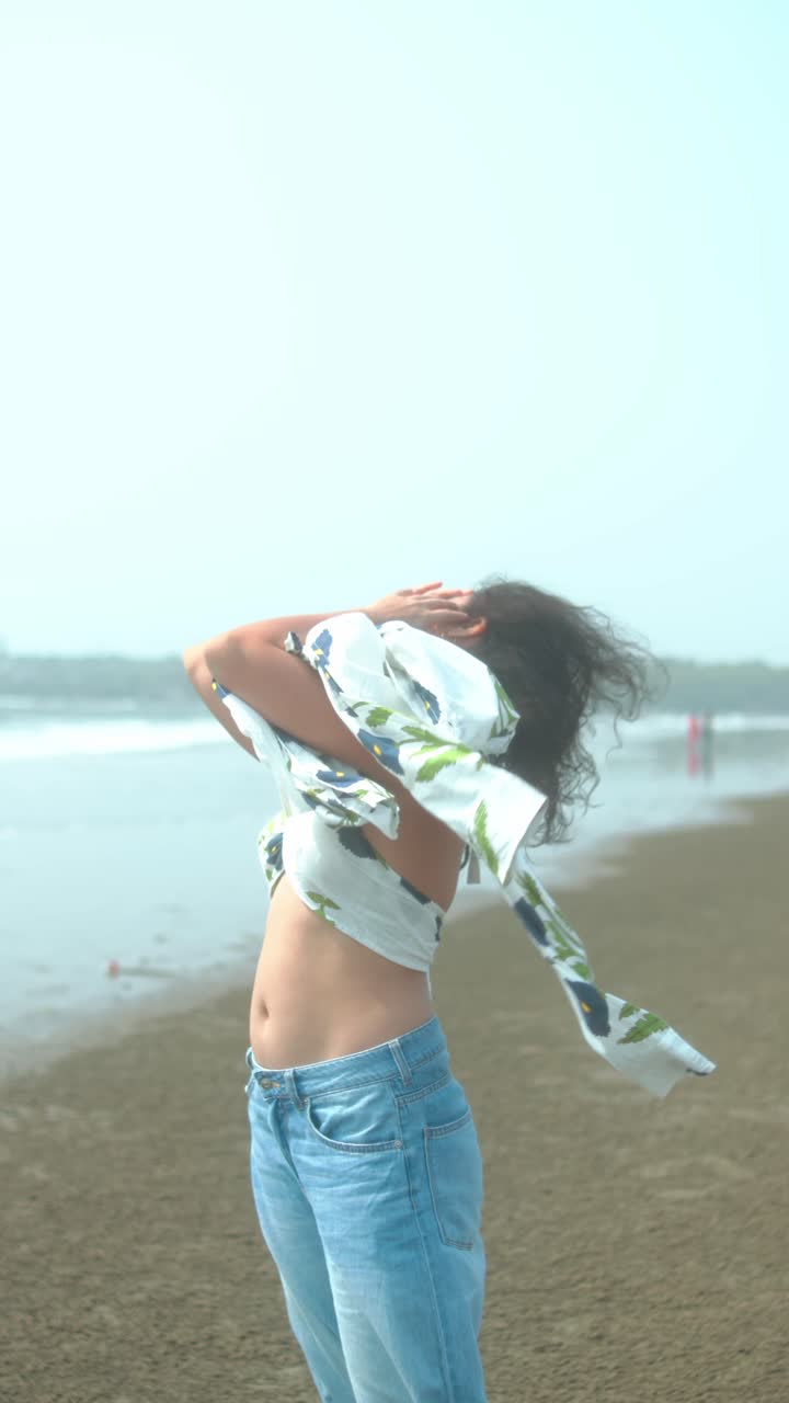 Confident young woman dancing at the beach in flowy clothes, summer mood and soft light