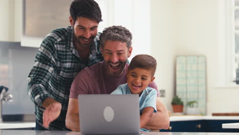 Same-Sex-Family-With-Two-Dads-And-Son-At-Home-In-Kitchen-Making-Video-Call-On-Laptop