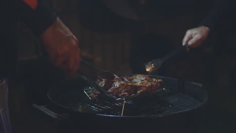 two men move cuts of lamb around the barbeque together with tongs