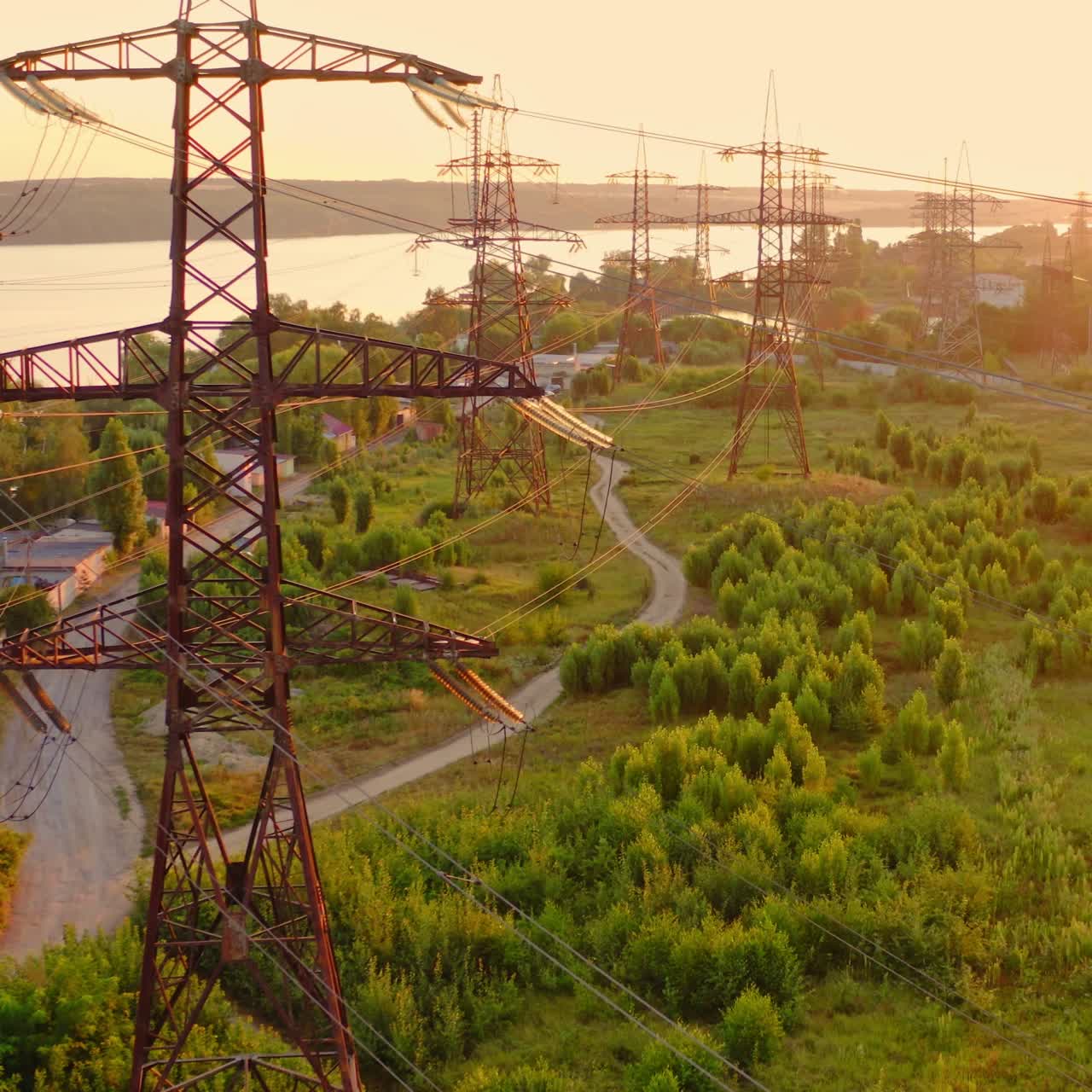 Transmission lines in the morning. High voltage electric lines near the river in summer. Tall electric towers at sunset. Aerial view. Slow motion.