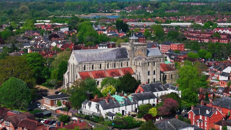 Ripresa aerea ravvicinata con drone dell'Abbazia di Romsey circondata da case, tetti e alberi nella storica città di Romsey, Hampshire, Inghilterra