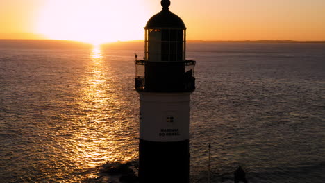 Aerial-view-of-Farol-da-Barra-illuminated-by-the-sun-and-the-sea,-at-sunset,-Salvador,-Bahia,-Brazil