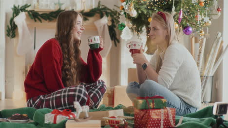 hermanas alegres hablando mientras sostienen tazas de café durante la navidad en casa