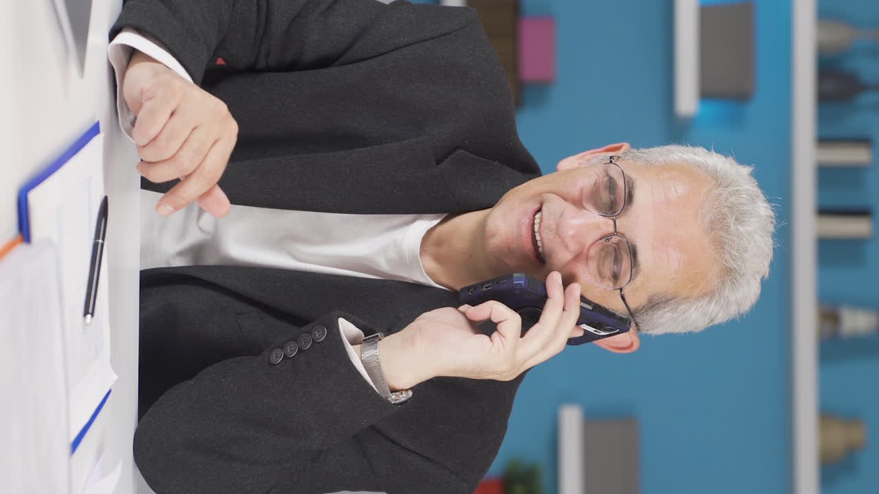 Vertical video of Home office worker man talking on the phone happily.
