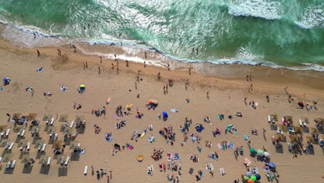 Aerial rising view from the beautiful Guincho beach full of people and the waves breaking on the seashore. Cascais,Portugal