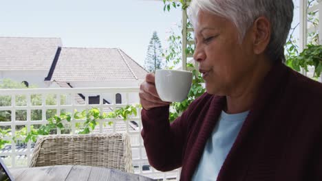 Feliz-Mujer-Senior-De-Raza-Mixta-Con-Portátil-Tomando-Café-Afuera