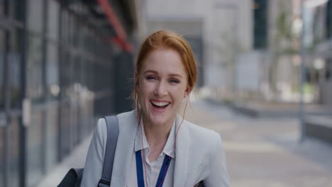 portrait-happy-young-red-head-business-woman-laughing-wearing-earphones-enjoying-relaxed-urban-lifestyle-listening-to-music-in-city-slow-motion