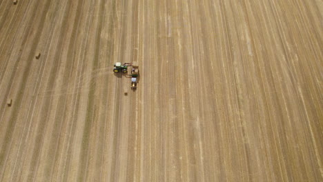 aerial top down of tractor loading hay bales on transporter after harvesting on wheat field in summer