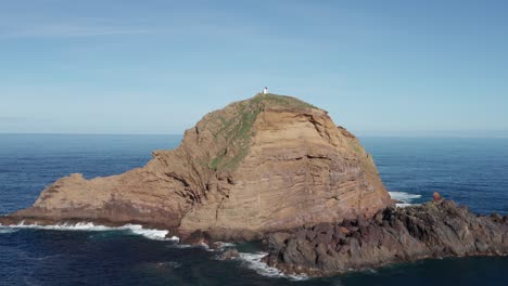 Epic-rock-in-ocean-with-small-lighthouse-on-top-during-sunny-day-with-vast-ocean-in-background-in-coastal-city-of-Porto-Moniz,-Madeira,-Portugal