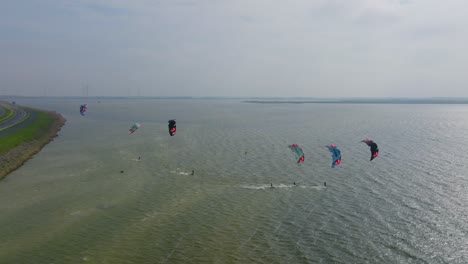 6-kitesurfers-riding-alongside-the-famous-Afsluitdijk-in-The-Netherlands,-drone-shot