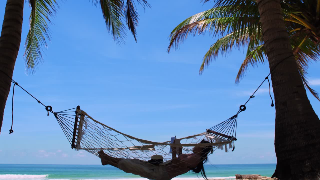 phuket, tailandia. mujer joven asiática relajándose con un libro en una hamaca junto a la playa al atardecer. mujer atractiva joven balanceándose en una hammock. vacaciones de vacaciones verano