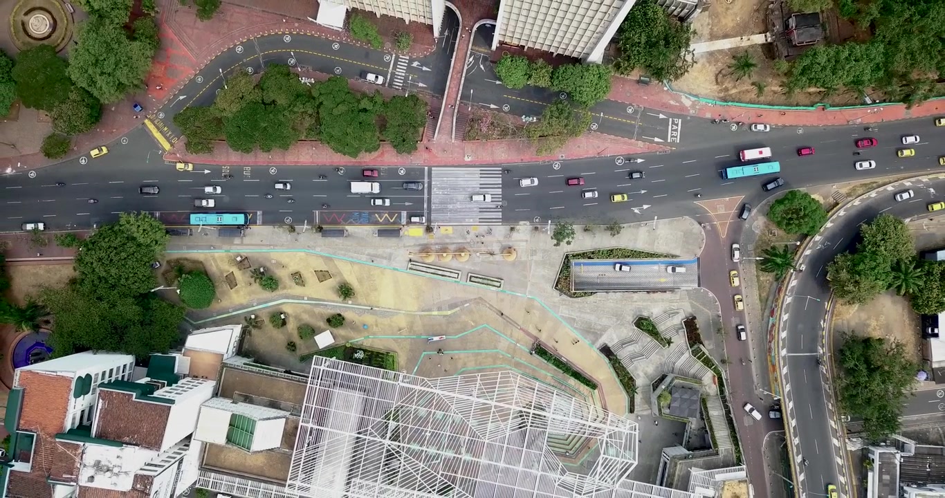 Vista aérea subindo do chão, mostrando carros circulando ao longo de uma rua principal em um dia típico na movimentada cidade de Cali, Colômbia