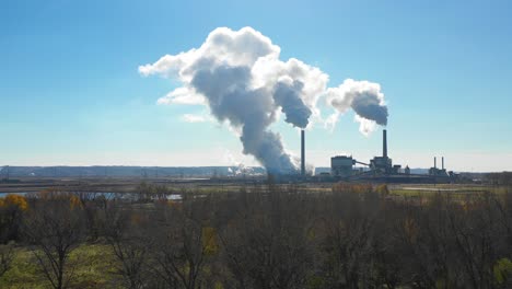 An aerial over a forest with huge polluting smokestacks belch CO2 into the atmosphere suggest pollution carbon emissions and global warming