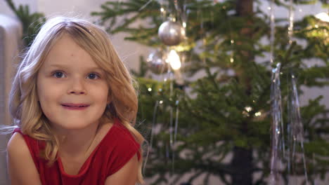 portrait of excited blonde girl by christmas tree waiting for santa claus in finland