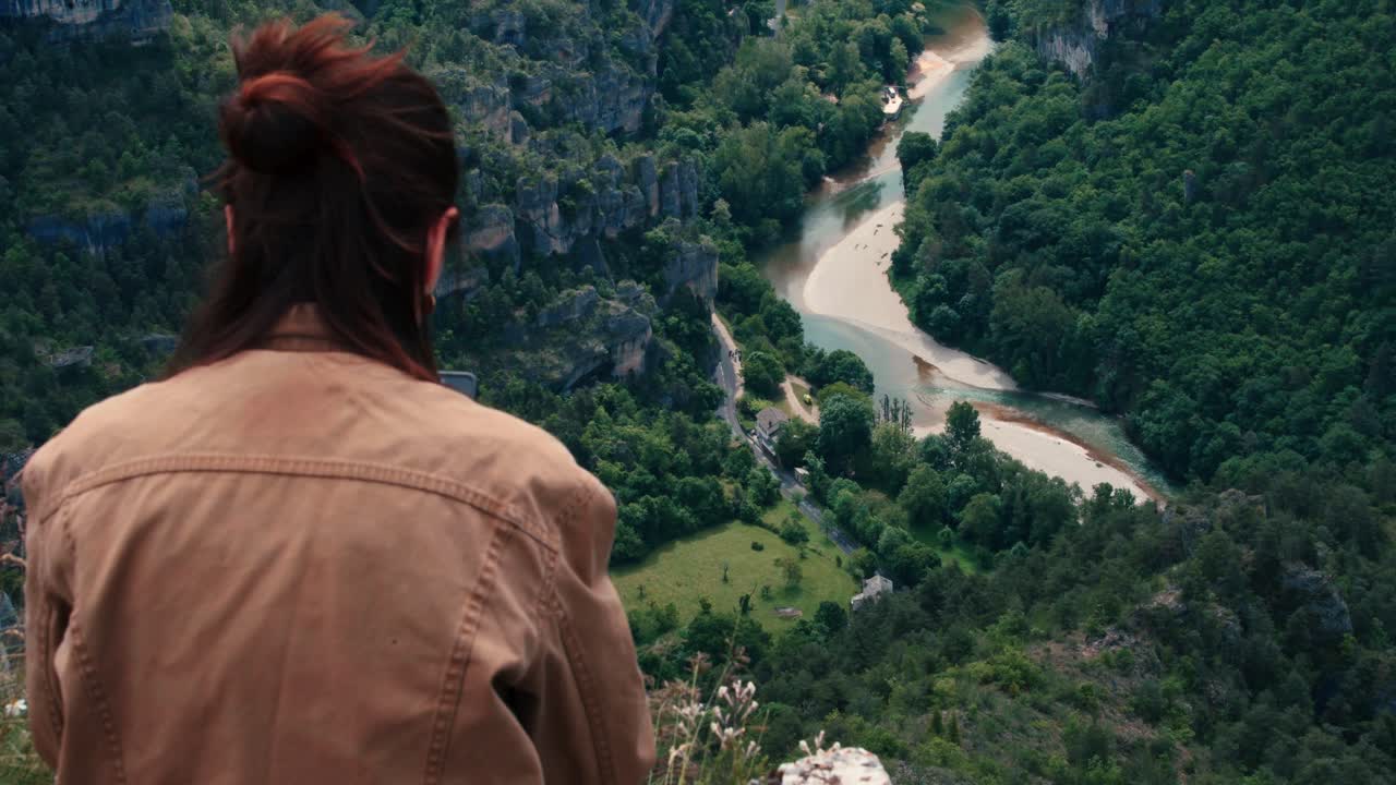 A woman stands quietly at the edge of a cliff, watching the canyon river below.