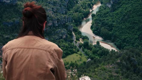 a woman stands quietly at the edge of a cliff, watching the canyon river below.