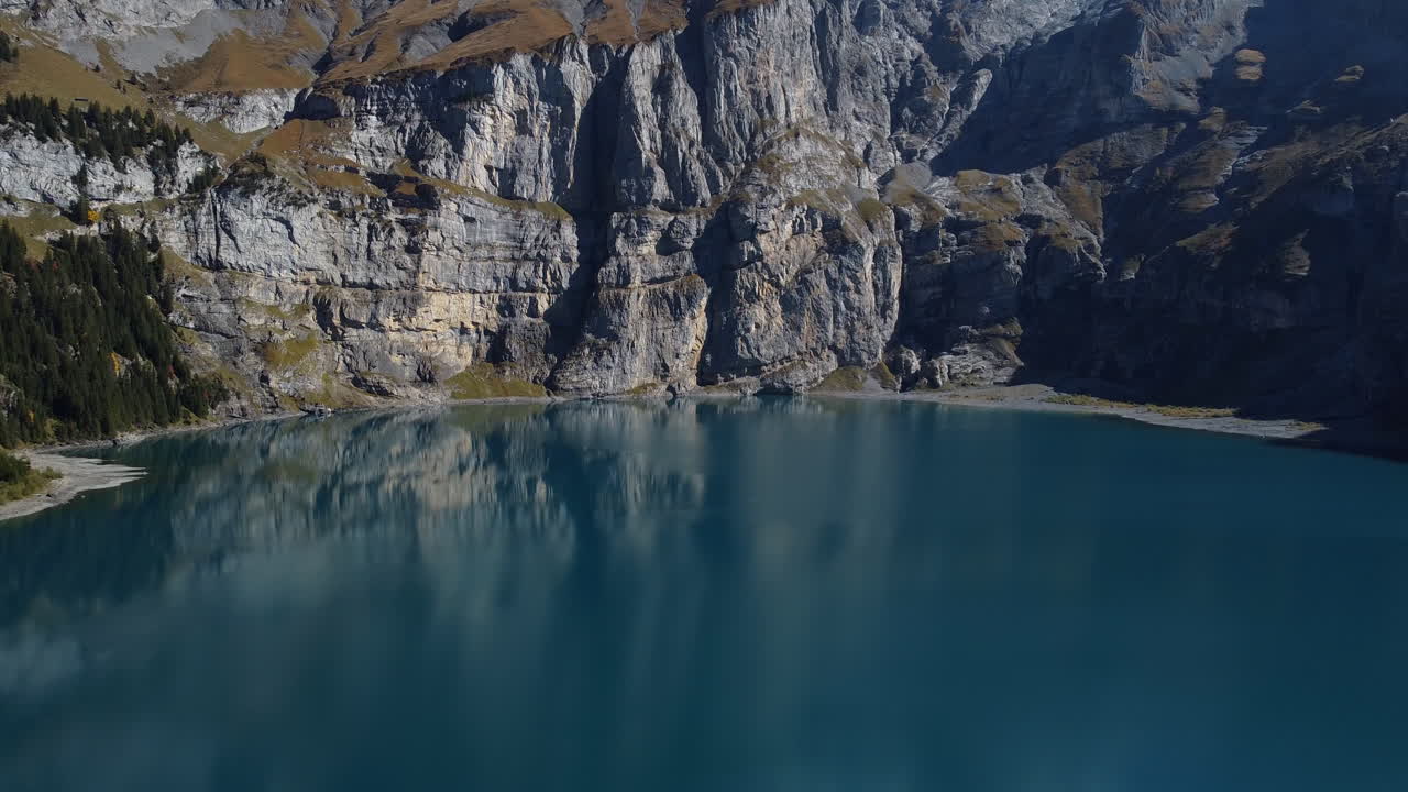toma aérea cinematográfica sobre el lago oeschinen y viendo el hermoso bosque y las montañas que lo rodean, en un día soleado y apreciando las aguas turquesas