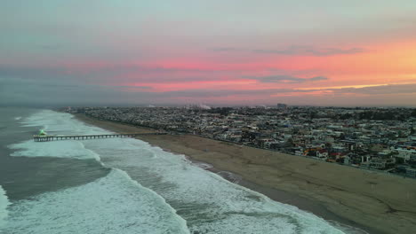 Impresionante-Puesta-De-Sol-Dorada-Sobre-La-Playa-De-Manhattan,-California,-Con-El-Muelle-Y-El-Acuario-Roundhouse-Al-Fondo