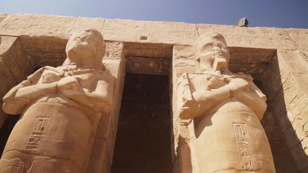 Tall statues of Pharoes in the Karnak Temple, Luxor Egypt. Carved details on the pillars and walls.
Slow movement towards the statues with a pan up.