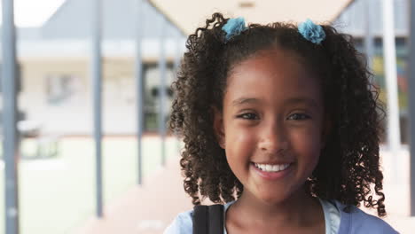 biracial girl with curly hair smiles at school, wearing blue hair ties, with copy space