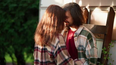 Close-up-shot-of-a-happy-brunette-guy-in-a-Green-checkered-shirt-hugging-his-brunette-girlfriend-in-a-checkered-shirt-near-green-coniferous-trees-Near-his-trailer-in-the-camp-during-a-picnic-in-the-summer